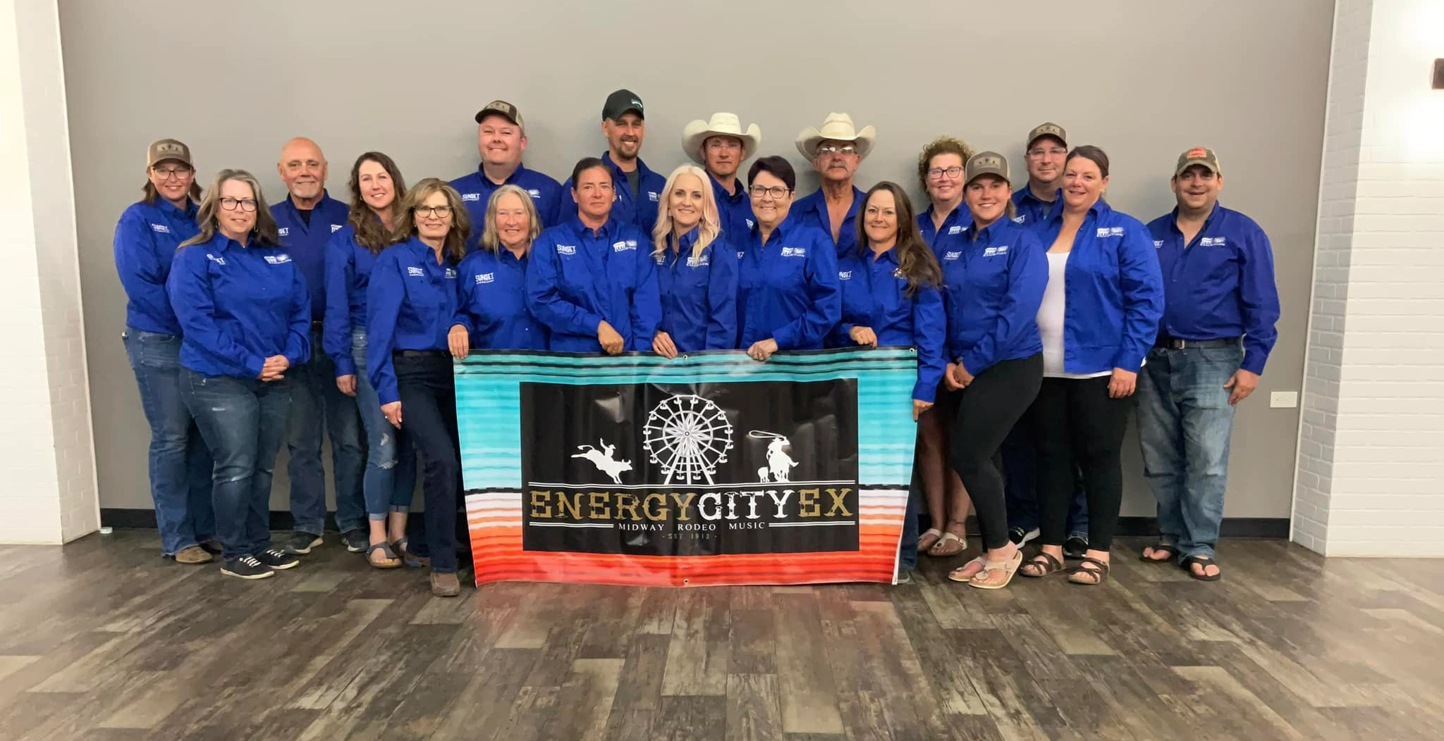 Group of people in blue jackets holding an "Energy City Ex" banner, posing together in a brightly lit indoor space.